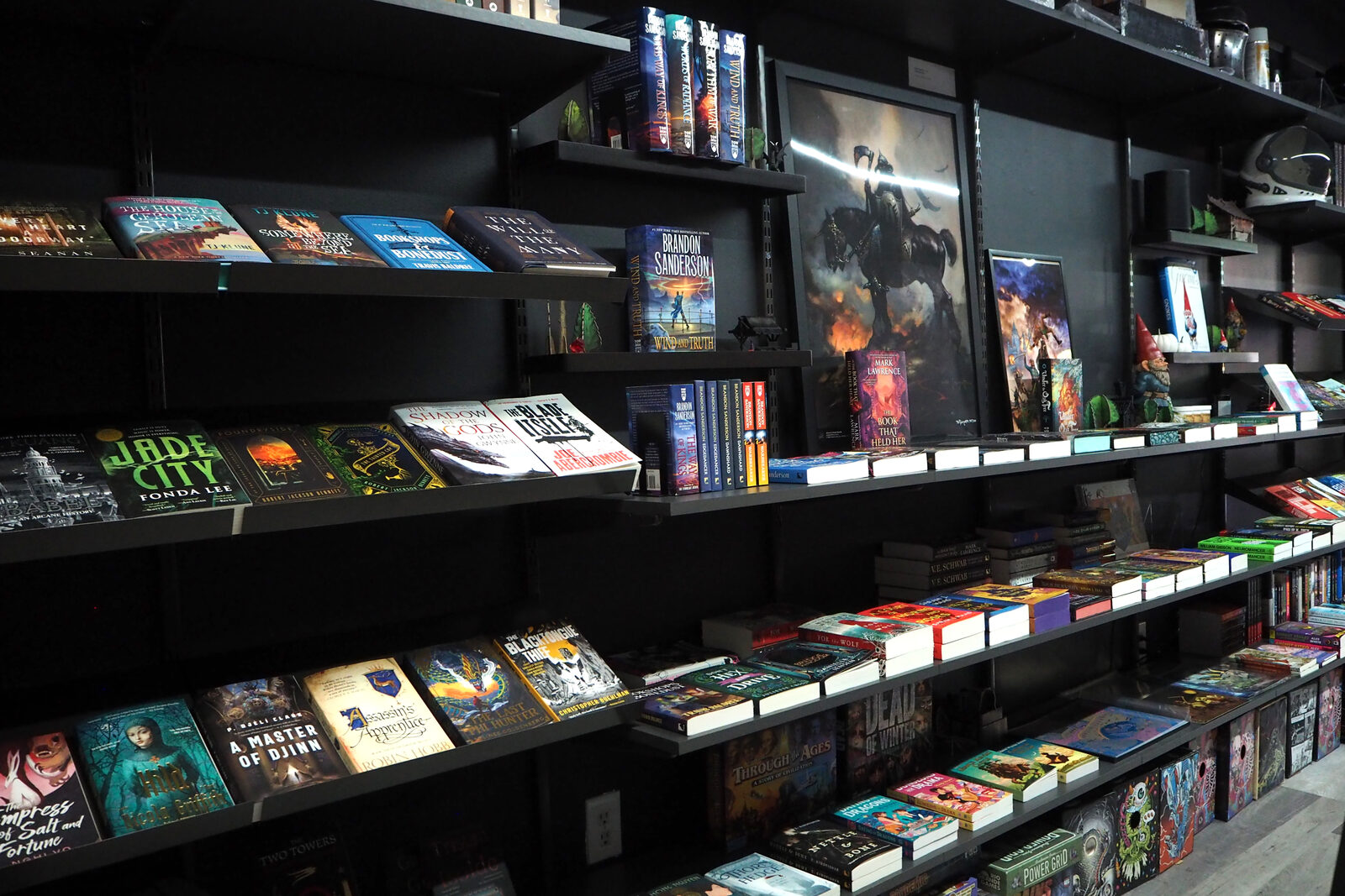 Close view of new sci-fi and fantasy face out on black shelves, a painting of a dark horseman hung among them